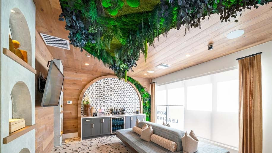 Modern leasing office with moss and preserved greenery on the ceiling, gray sofa, and large windows.